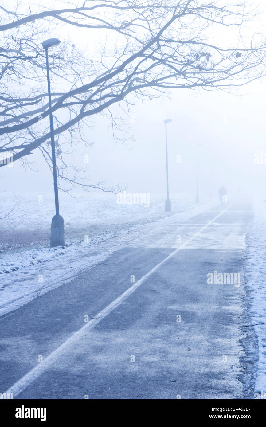 Straße in einem nebligen Wintertag mit einer schwachen Figur Mit dem Fahrrad Stockfoto