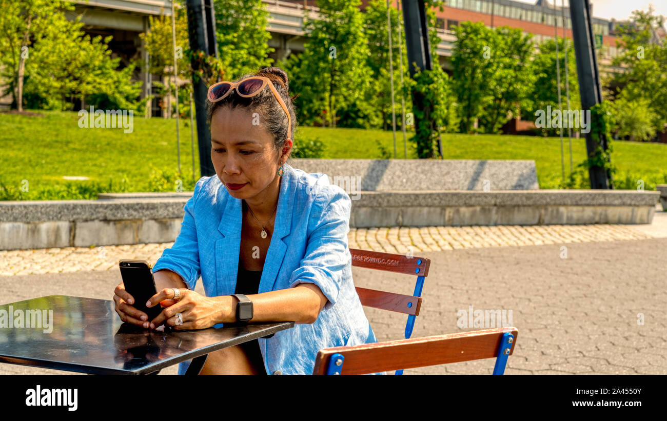 Asiatische Frau mit blauen Blazer und Anhänger im Cafe sitzen mit mobilen phonein ihre Hand Stockfoto