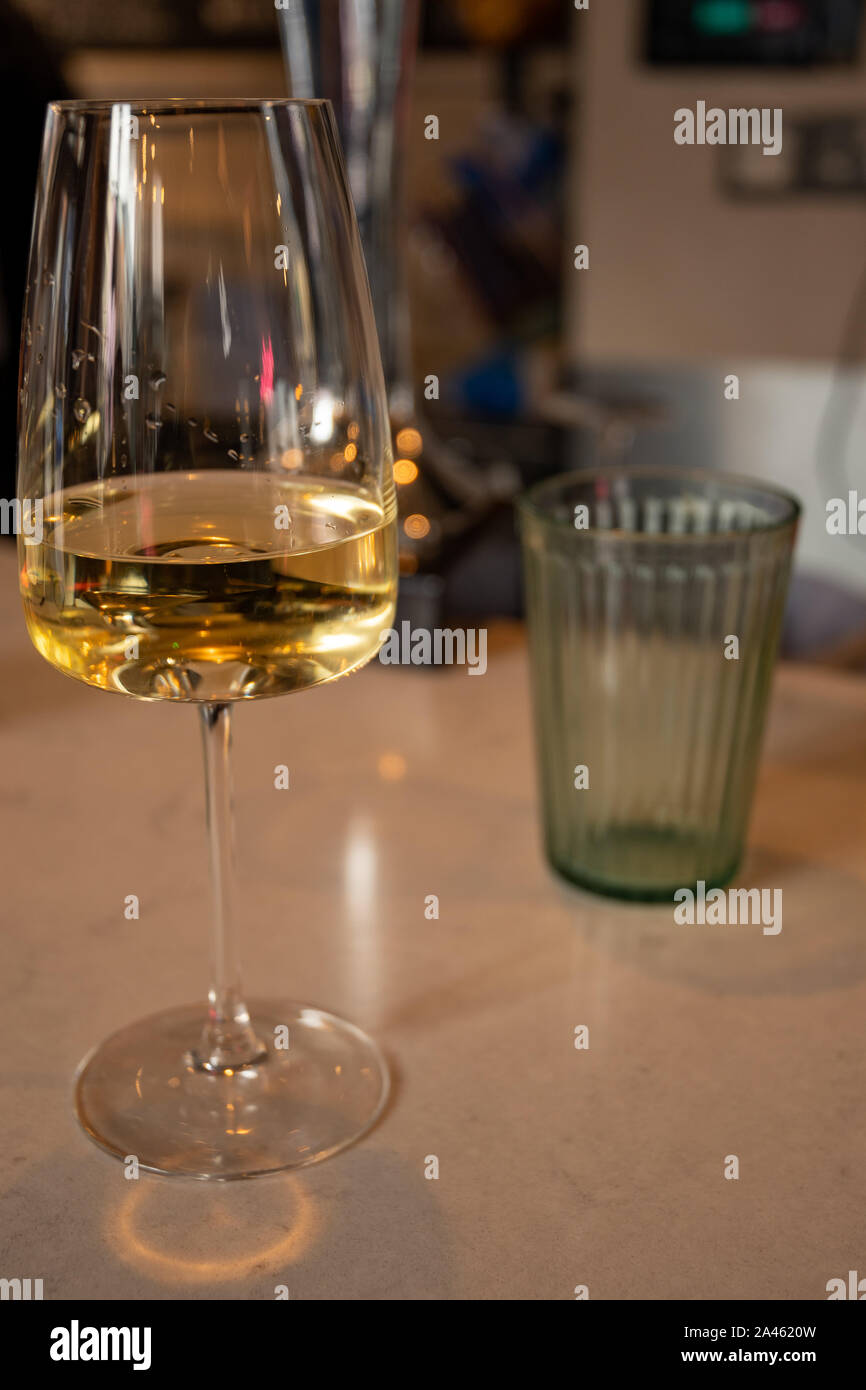 Aufnahme eines Restaurantthekens mit einem Glas Weißwein aus der Nähe und einem unfokussten Blick auf eine moderne Location im Hintergrund. Stockfoto