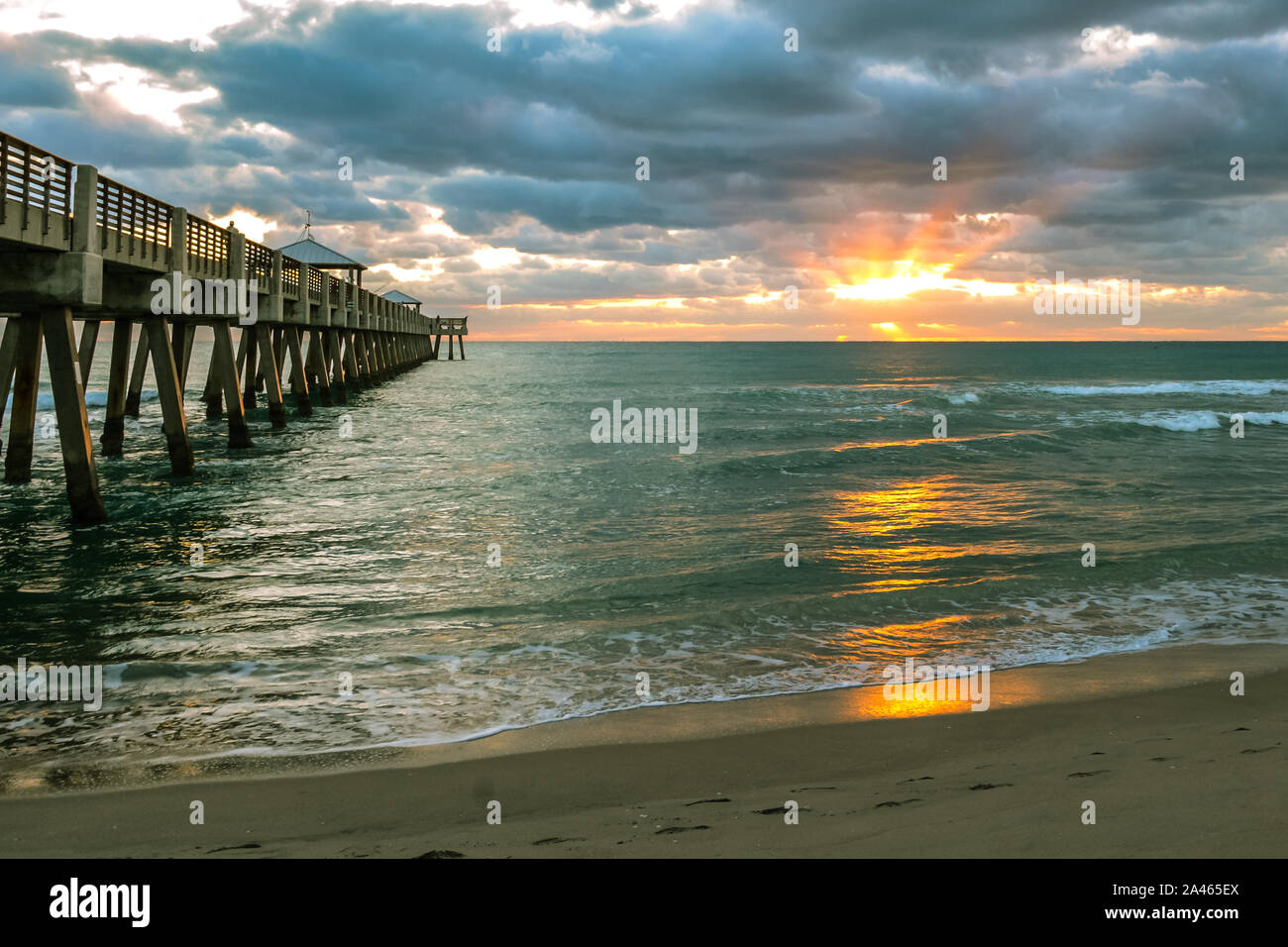 Sonnenstrahlen am Horizont aus Juno Beach, Florida, mit der konkreten Fishing Pier gebaut in den Atlantischen Ozean. Stockfoto
