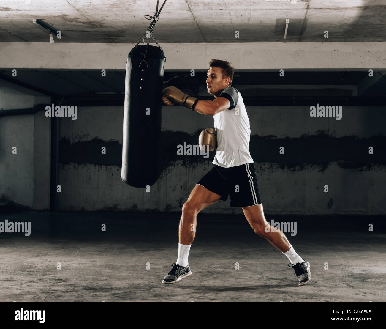 Entschlossene junge Muay Thai Kämpfer Boxhandschuhe Thai Boxing Training mit Boxsack Stockfoto