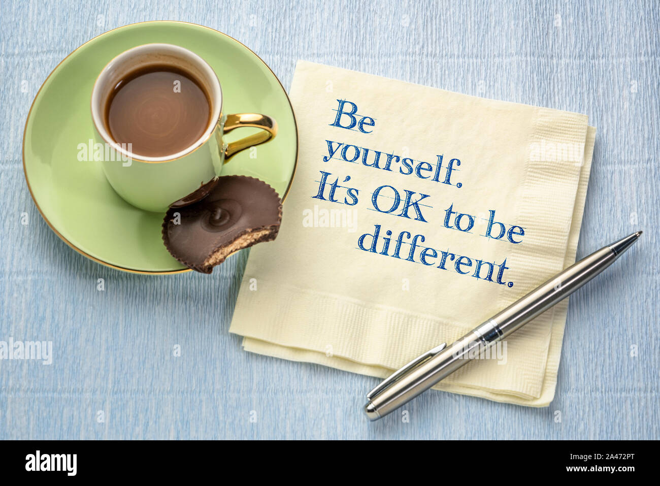 Werden Sie sich. Es ist in Ordnung, anders zu sein. Inspirational Anführungsstrich auf eine Serviette mit einer Tasse Kaffee, die persönliche Entwicklung, und Selbstverbesserung Konzept. Stockfoto
