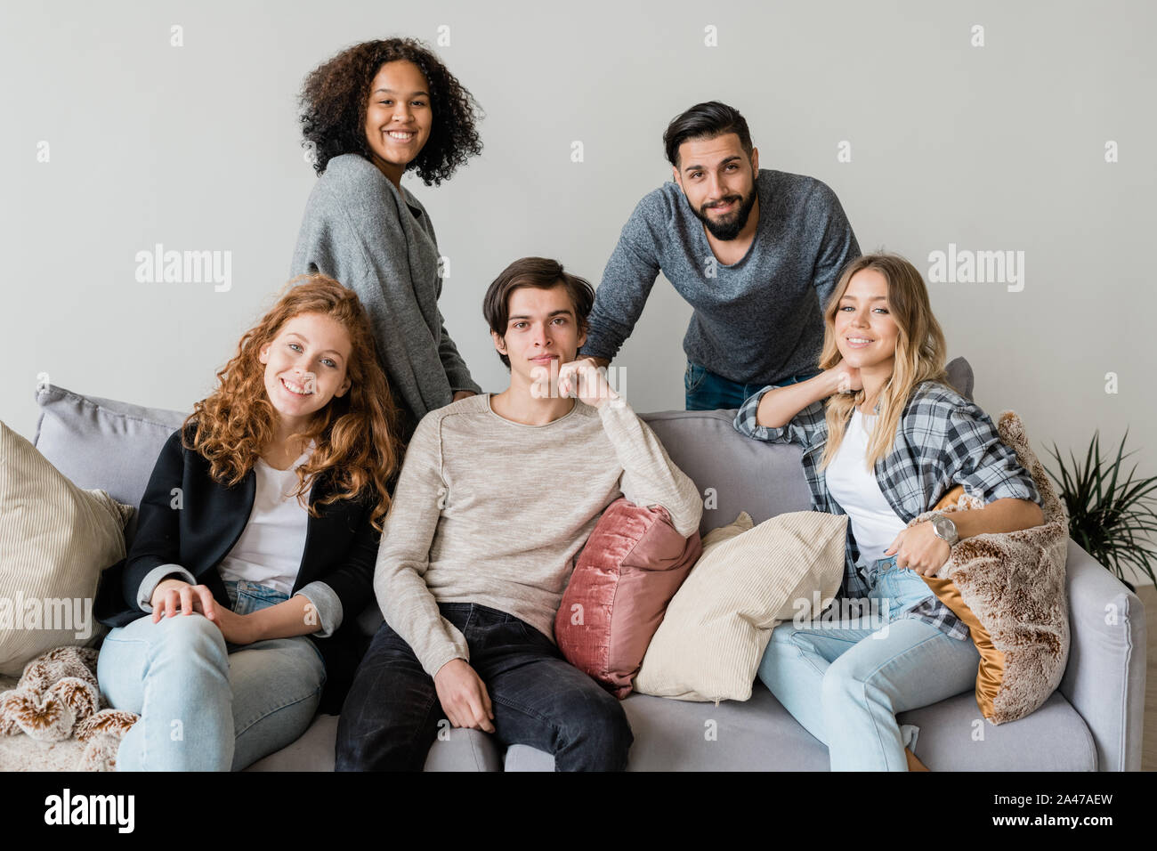 Gruppe der glückliche junge interkulturelle Freunde in casualwear entspannend auf weichen Couch Stockfoto