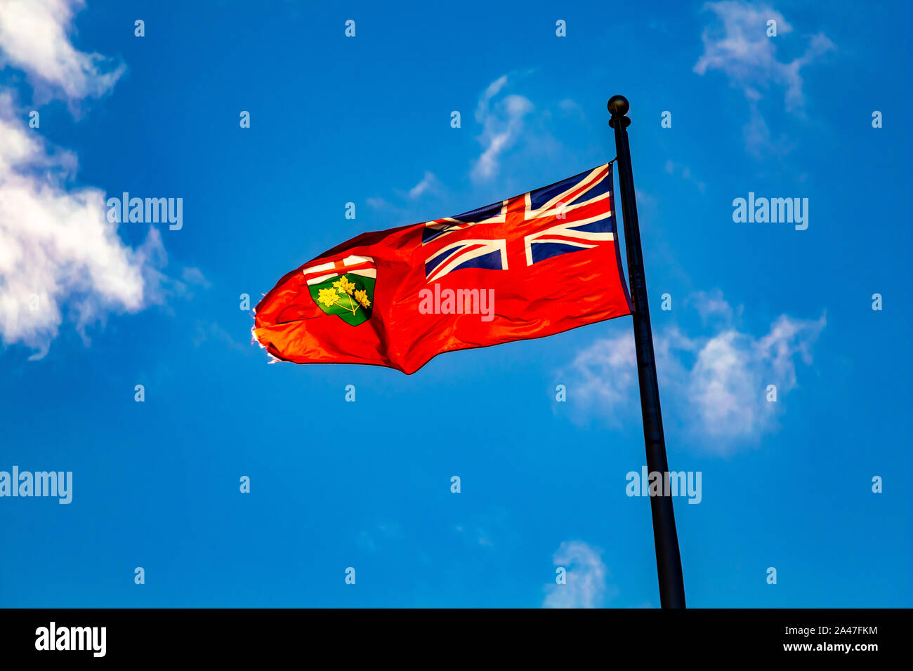 Die Flagge der kanadischen Provinz Ontario fliegt im Wind vor blauem Himmel. Er bläst, links neben dem Fahnenmast vor einem strahlend blauen Himmel. Stockfoto