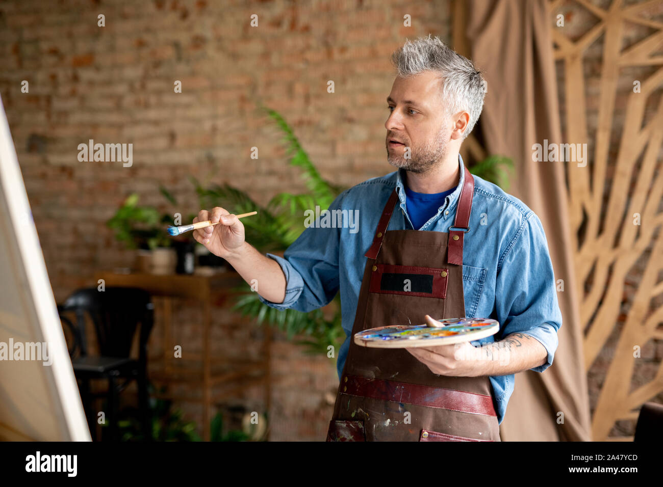 Maler mit Pinsel und Palette an unfertigen Malerei inspiriert Stockfoto