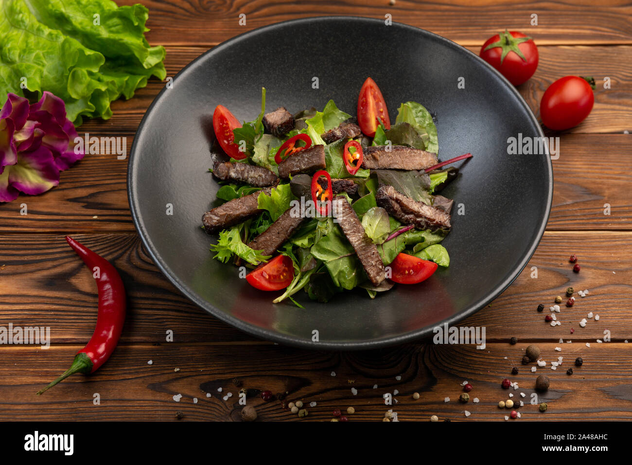Thai Beef Salad gebackenes Kalbsfilet, Salat mischen, Kirsche, Chili mit Olivenöl in einer schwarzen Platte auf einem hölzernen Hintergrund Stockfoto
