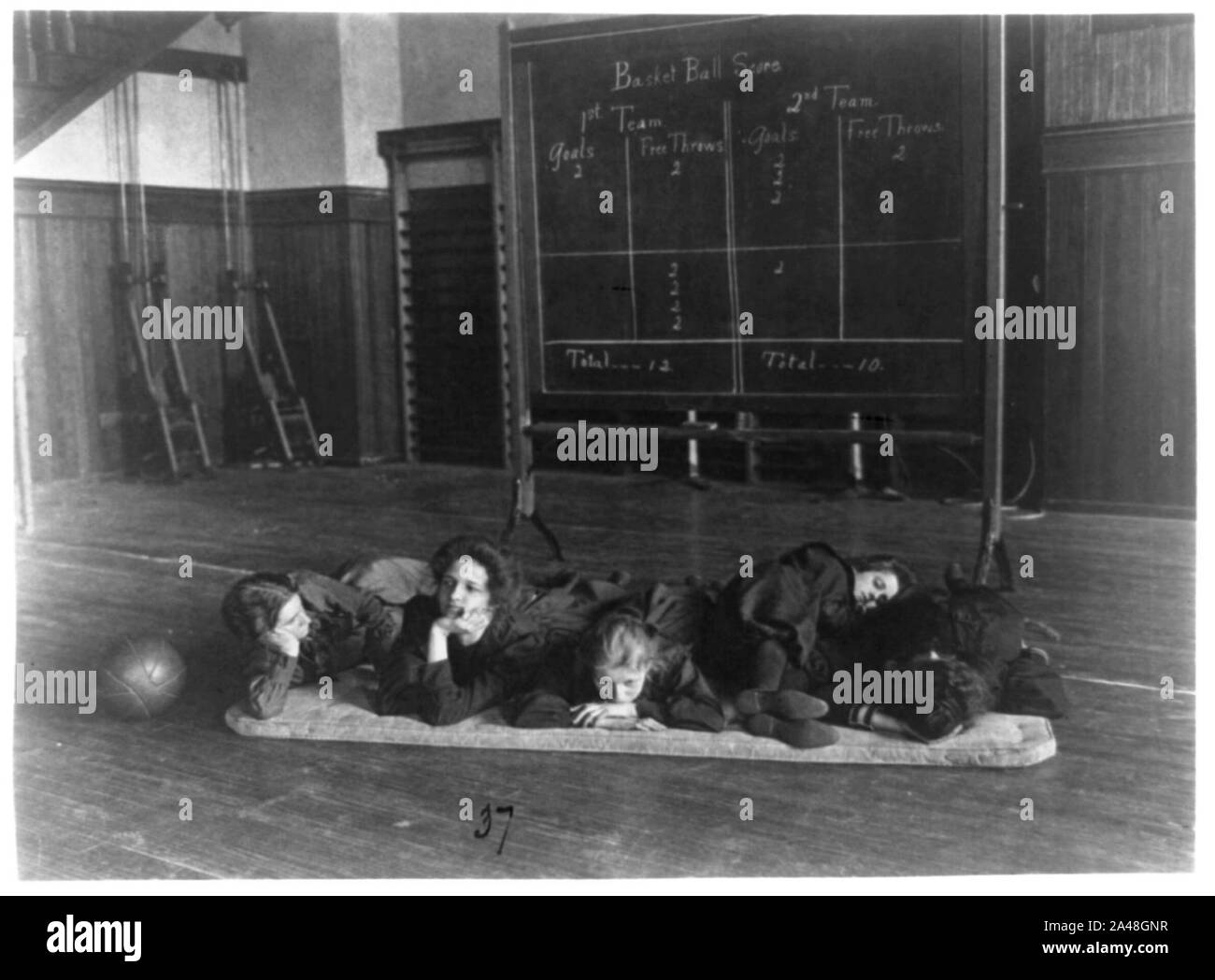 Fünf Mädchen liegen auf Matten in der Turnhalle vor Basketball scoreboard, Western High School, Washington, D.C. Stockfoto