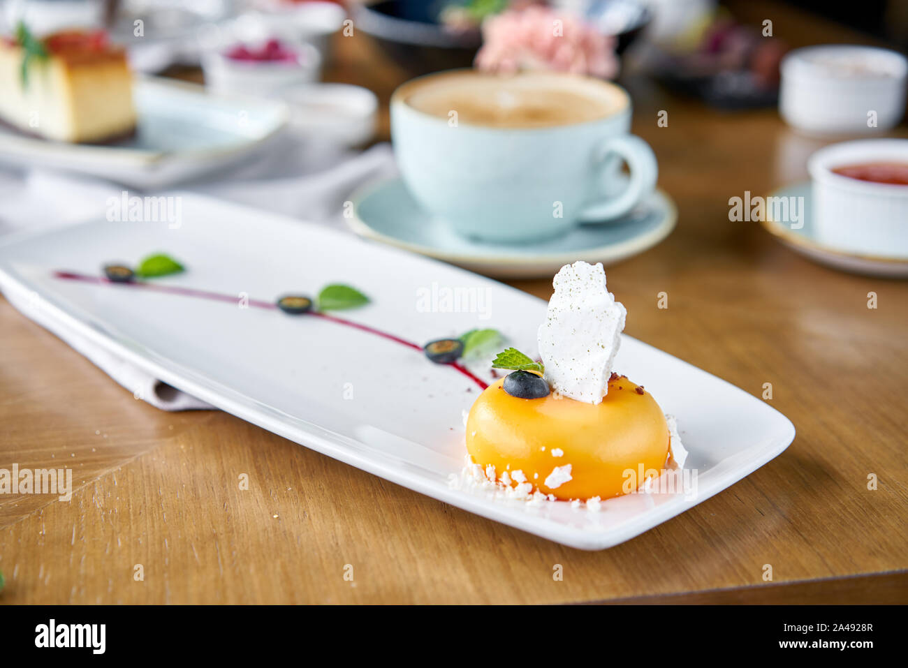 Gelbe mousse-Kuchen. Frühstück im Café, Kaffee am Morgen. Cappuccino und viele Desserts auf dem Tisch. Französische Dessert, Blaubeere, Minze und ein Stück Stockfoto