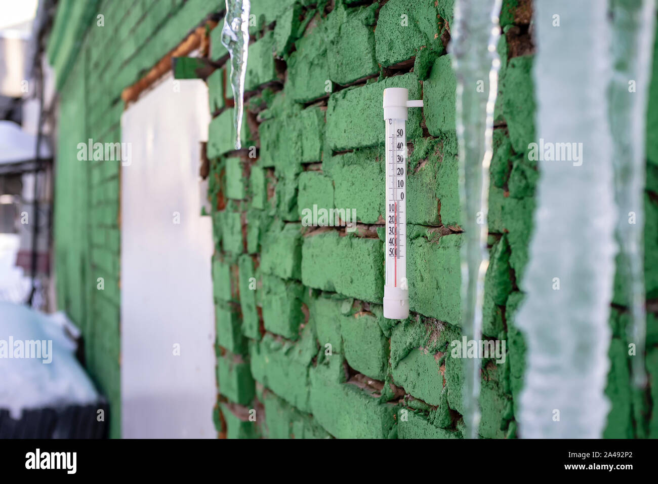 Quecksilber Thermometer hängen an einer grünen Wand, Eiszapfen vom Dach hängend während ein tauwetter Stockfoto