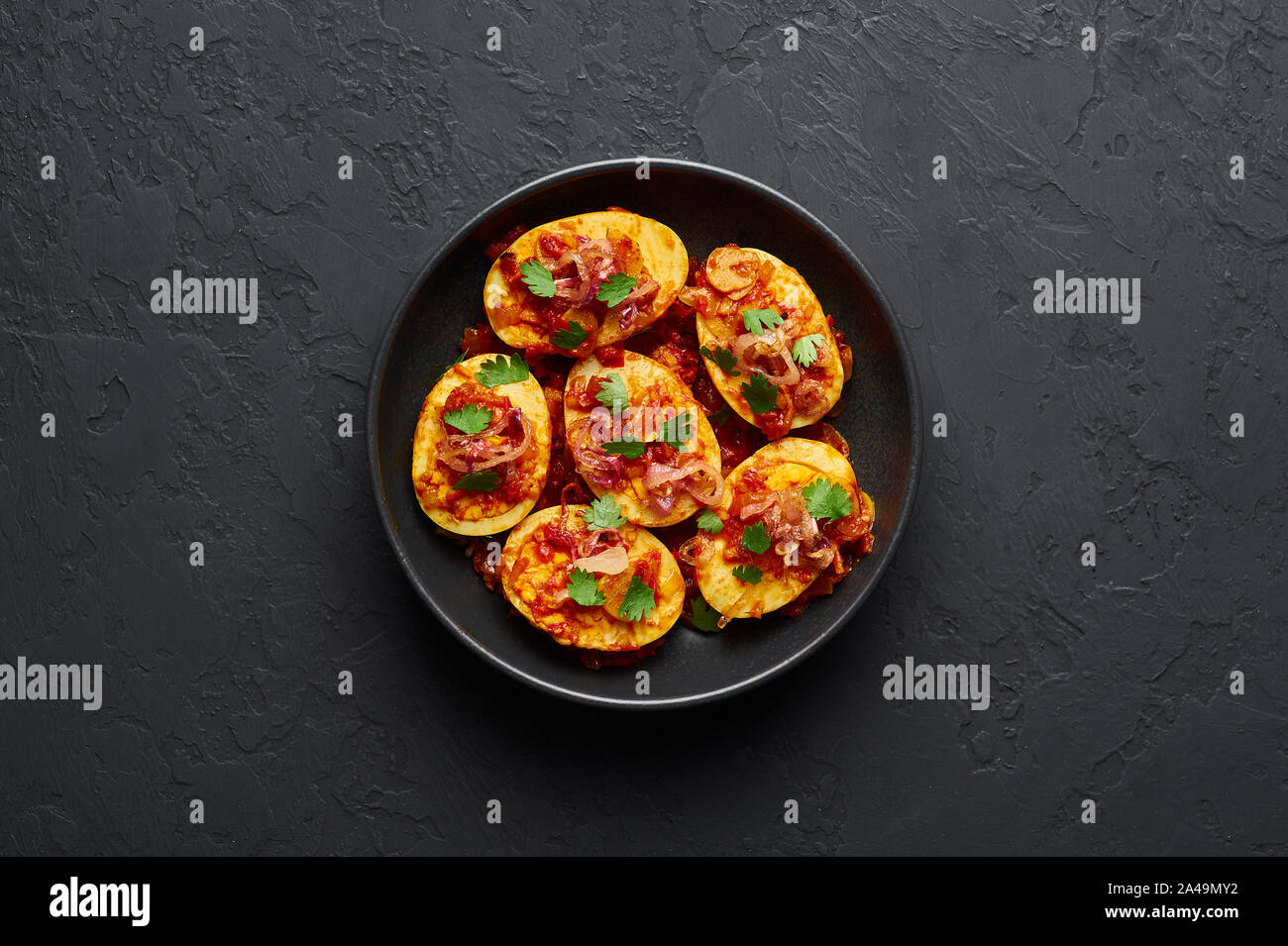 Goldene Ei Curry in schwarz Schüssel am dunklen Schiefer Hintergrund. Die burmesische Ei Curry ist beliebt Myanmar Küche Teller mit Ente oder Huhn Eier, Tomaten, Ingwer Stockfoto