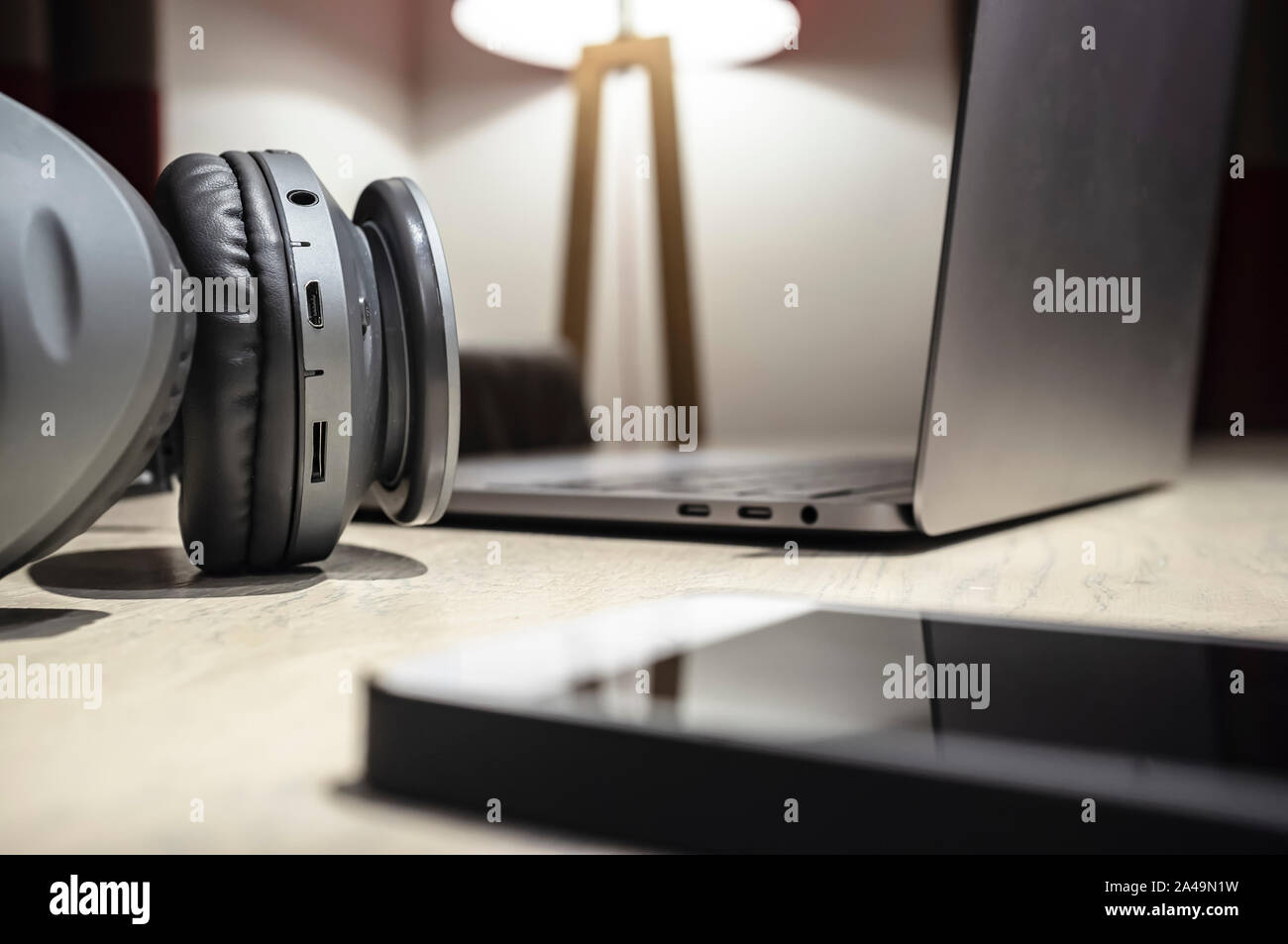 Kopfhörer, ein Laptop und ein Handy liegen auf einem hölzernen Tisch in einer gemütlichen Atmosphäre. Musikalische Konzept. Close-up. Stockfoto