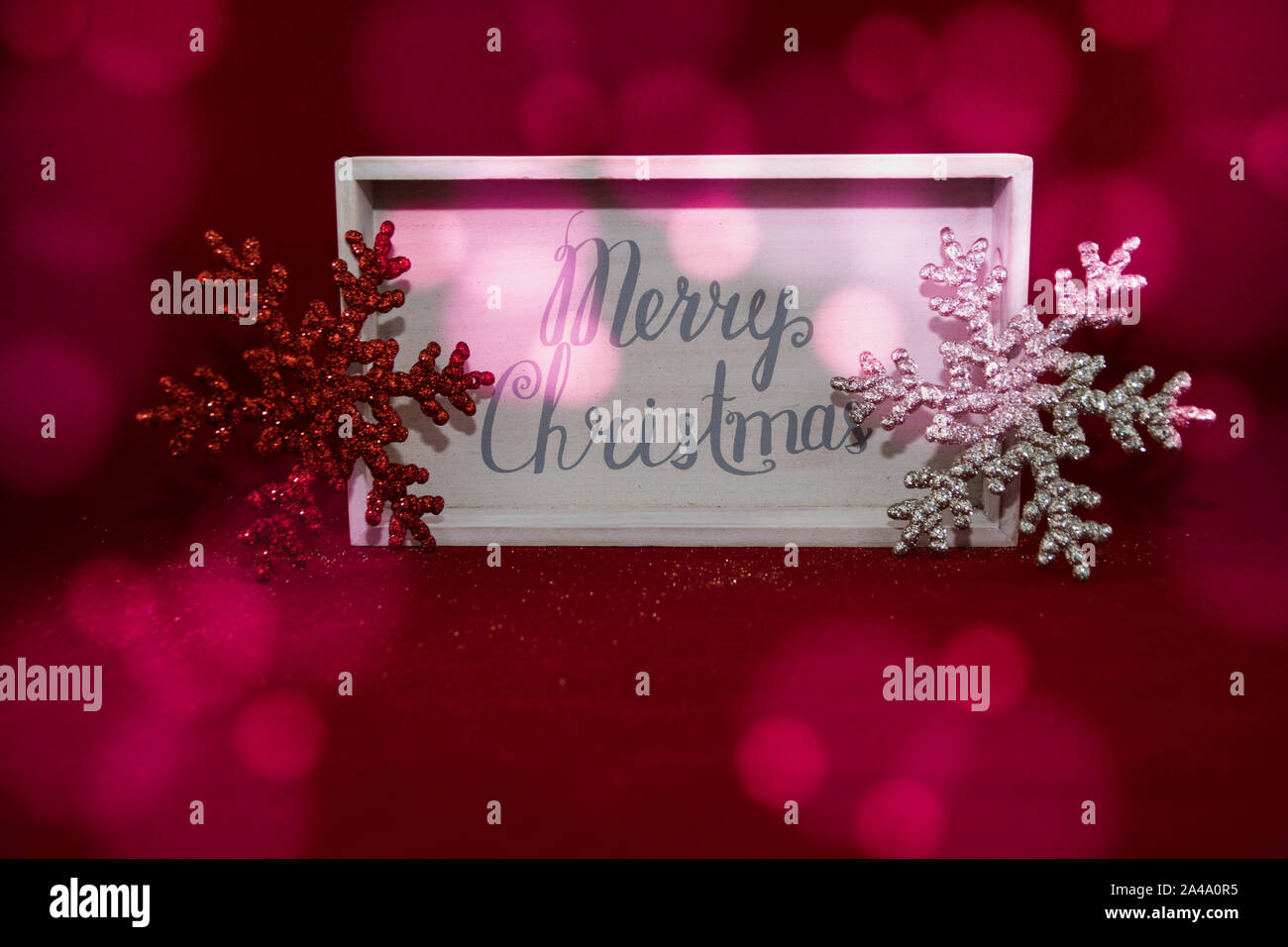 Holzkiste mit Frohe Weihnachten mit Rot und Silber Schneeflocke jeder Seite. Roter Hintergrund mit Licht. Flache Perspektive. Stockfoto