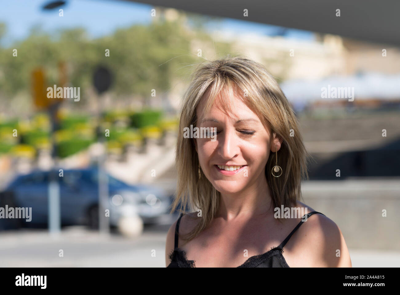 Closeup Portrait einer blonden Frau, die Augen geschlossen, während lächelnd im Freien an einem sonnigen Tag Stockfoto