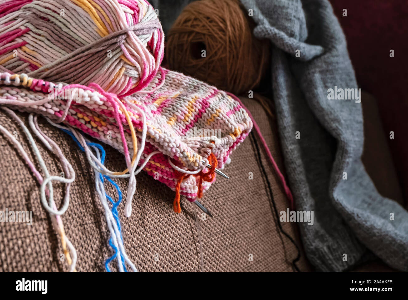 Bunte Wolle Garn und Stricknadeln und das fertige Produkt auf dem Sofa. Close-up. Stockfoto