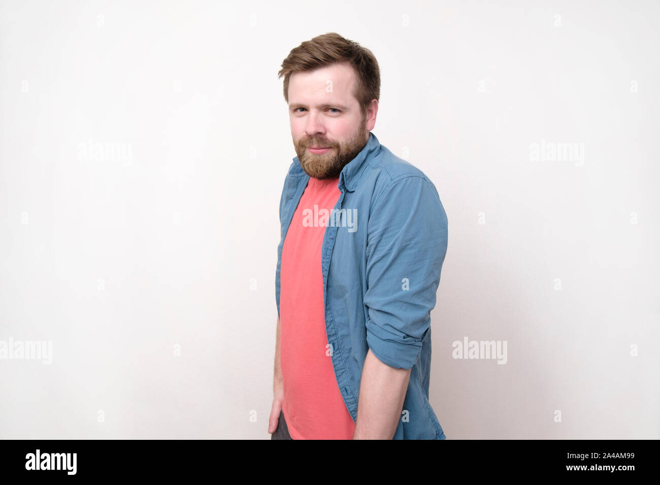 Schüchtern, in Liebe Mann hob die Schultern, legte die Hände in den Taschen und starrt angestrengt lächelnd. Auf weissem frne isoliert. Close-up. Stockfoto