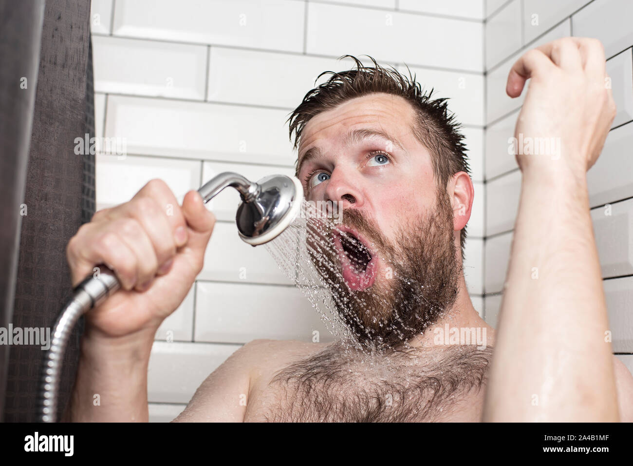 Cute bärtiger Mann singen im Badezimmer mit der Dusche mit fließendem Wasser anstelle von einem Mikrofon. Close-up. Stockfoto