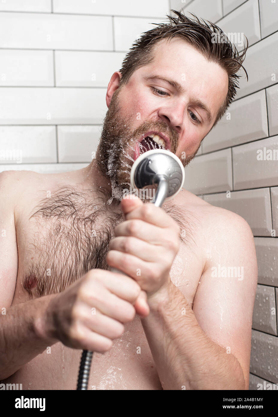 Cute bärtiger Mann singen im Badezimmer mit der Dusche mit fließendem Wasser anstelle von einem Mikrofon. Vertikale Foto. Close-up. Stockfoto