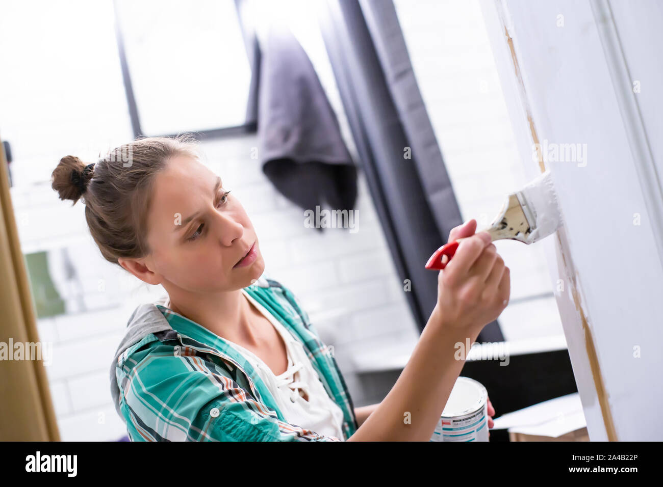 Home Reparaturen. Eine fokussierte Frau malt in Weiß der Eingang zum Badezimmer mit einer Bürste und kann, hält sie in den Händen. Close-up. Stockfoto