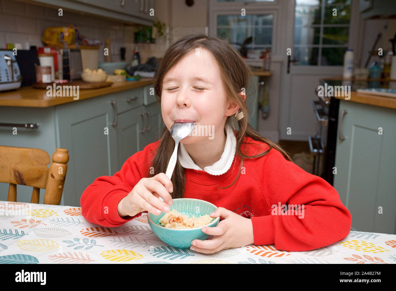 Junges Mädchen mit Milchreis am Küchentisch Stockfoto