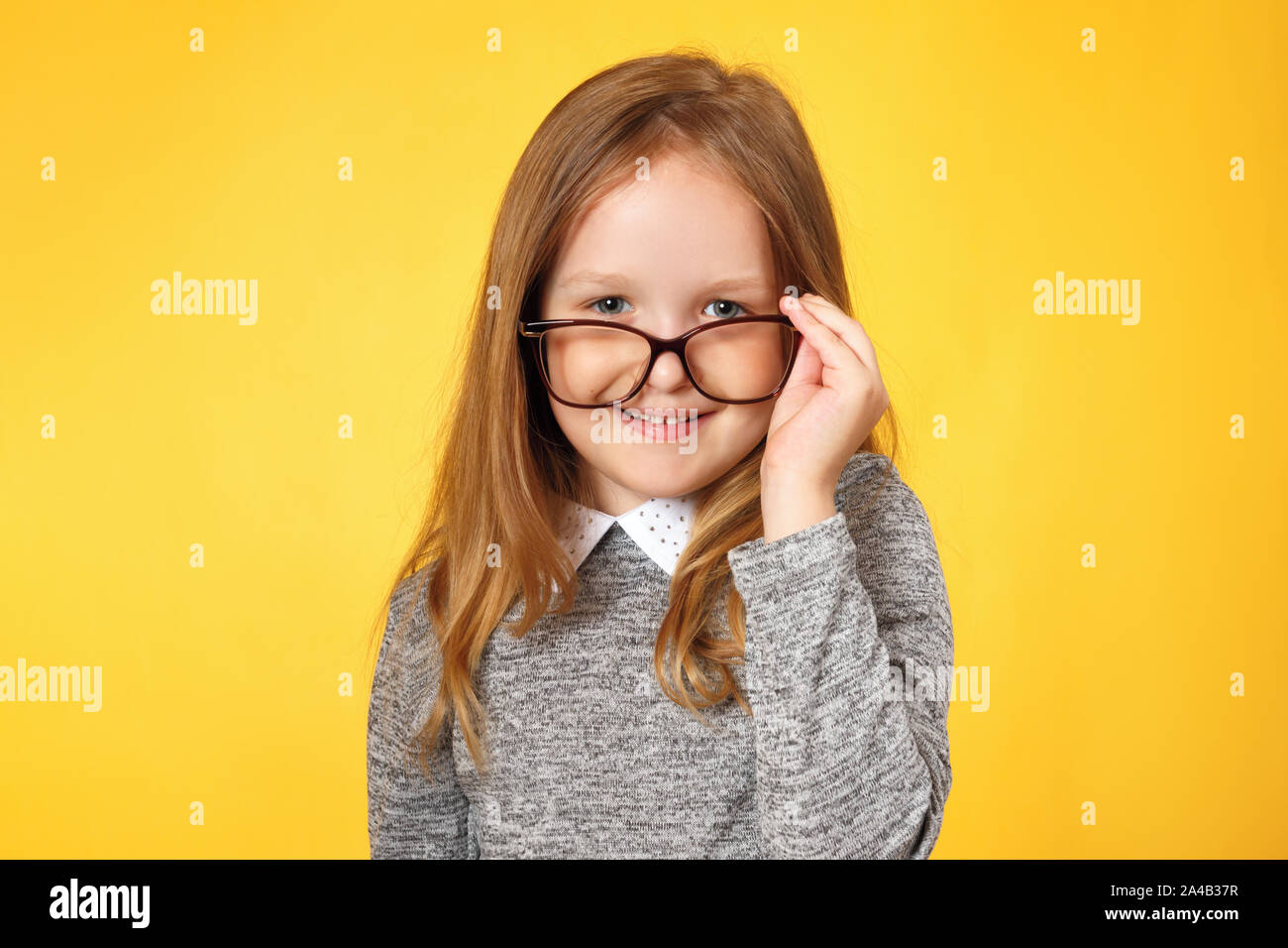 Kluges Mädchen Schulmädchen mit Brille. Ein Kind in einem grauen pullover auf gelbem Hintergrund. Stockfoto