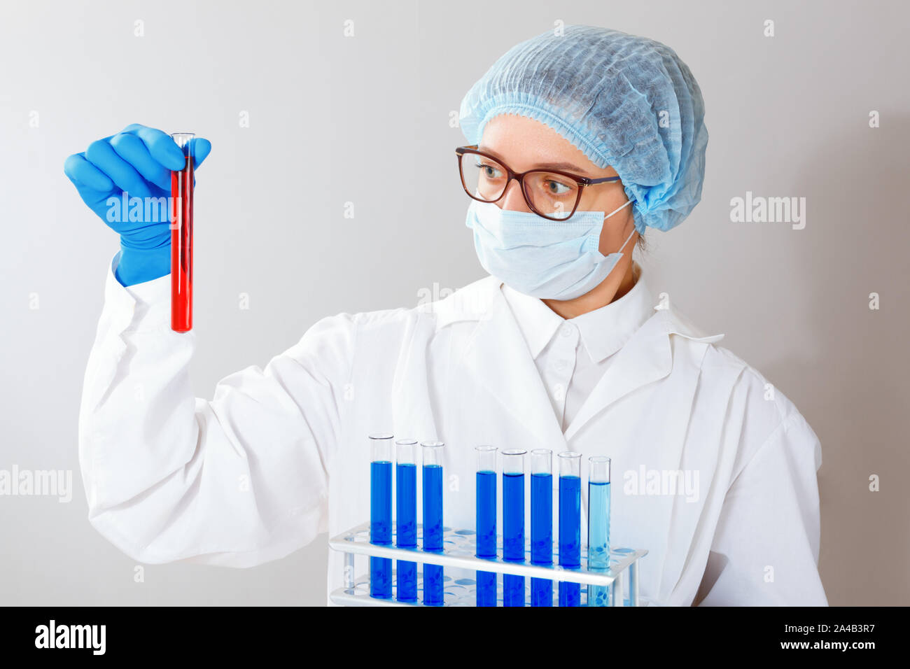 Eine Wissenschaftlerin, ein Apotheker, ein Medic mit Brille, ist Experimentieren im Labor und hält ein Reagenzglas mit roter Flüssigkeit in seiner Hand. Stockfoto