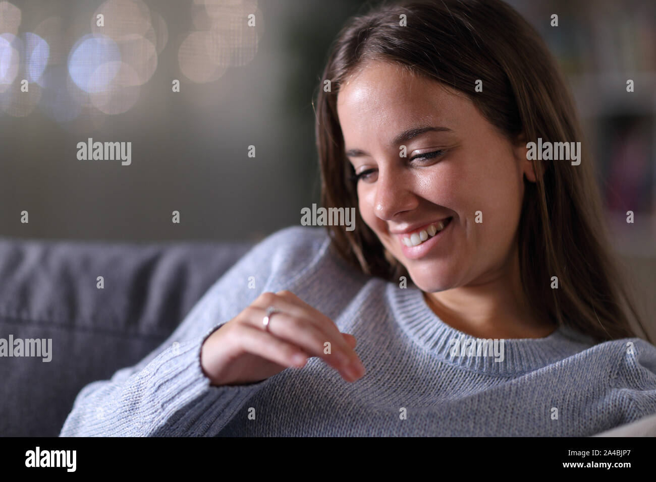 Glückliche Braut an Engagement Ring sitzen auf einer Couch im Wohnzimmer in der Nacht zu Hause suchen Stockfoto