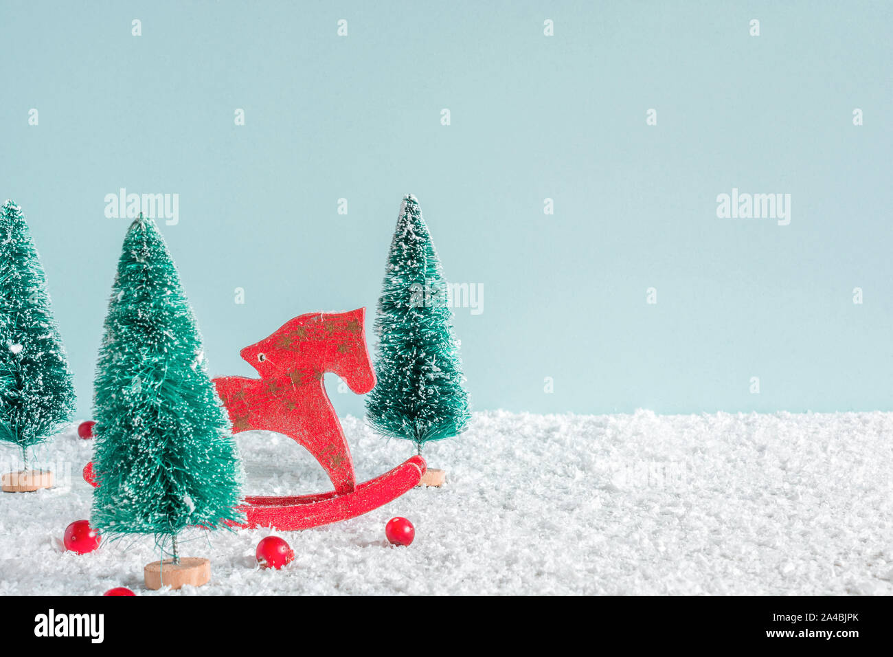 Weihnachten Hintergrund. Tannen mit Pferd, Spielzeug und roten Beeren auf Schnee Hintergrund. Kreative Weihnachtskarte mit Kopie Raum Stockfoto
