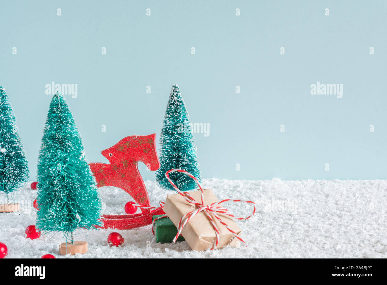 Weihnachten Hintergrund. Tannen mit Pferd, Spielzeug, Geschenkboxen und roten Beeren auf Schnee Hintergrund. Kreative Weihnachtskarte mit Kopie Raum Stockfoto