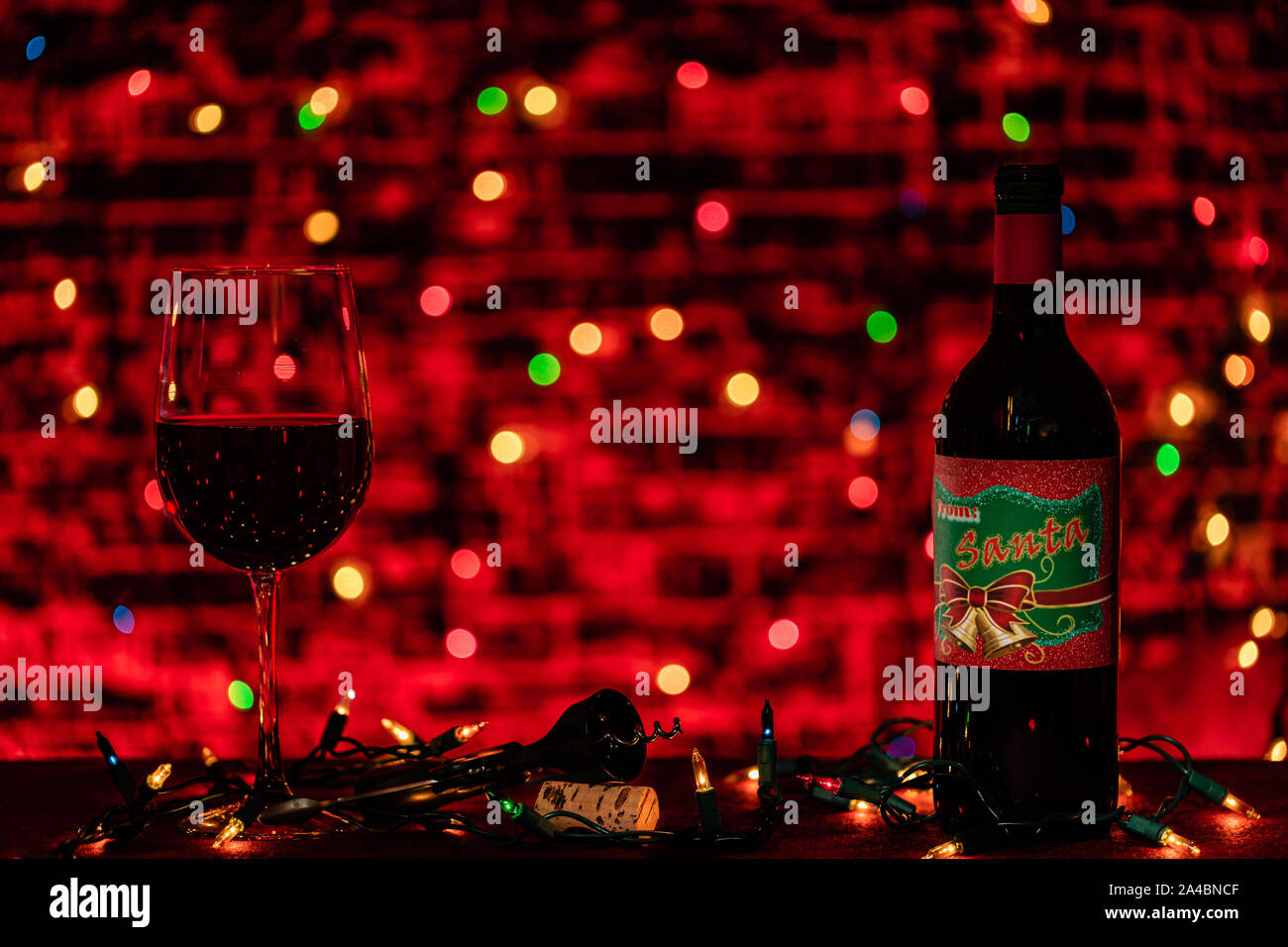 Eine warme düster beleuchteten Szene der ein Glas und eine Flasche Wein bereit für einen Urlaub Feier. Die Beleuchtung ist die Weihnachtsbeleuchtung erzeugen ein warmes Licht. Stockfoto