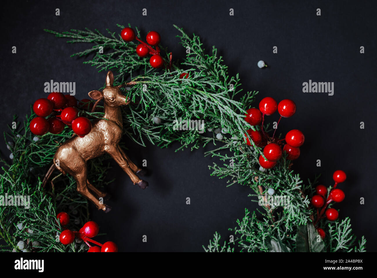 Weihnachten Kranz Detail der immergrünen, roten Beeren und gold Rentier auf dunklem Hintergrund. Nandian Netzwerk grüner Zweig und rustikalen Krone. Flach. Stockfoto