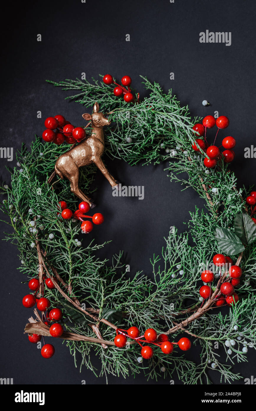Weihnachten Kranz Detail der immergrünen, roten Beeren und gold Rentier auf dunklem Hintergrund. Nandian Netzwerk grüner Zweig und rustikalen Krone. Flach. Stockfoto