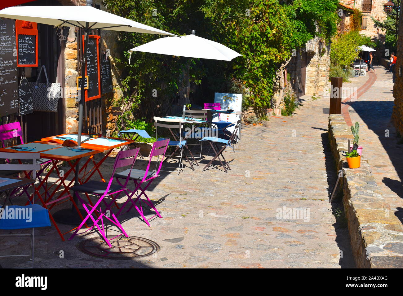 Familienbetrieb organic Restaurant auf einer Straße mit Kopfsteinpflaster in einem mittelalterlichen französischen Stadt. Bunte Tische, Stühle, weiße Sonnenschirme und Menüs auf einer Steinmauer. Stockfoto