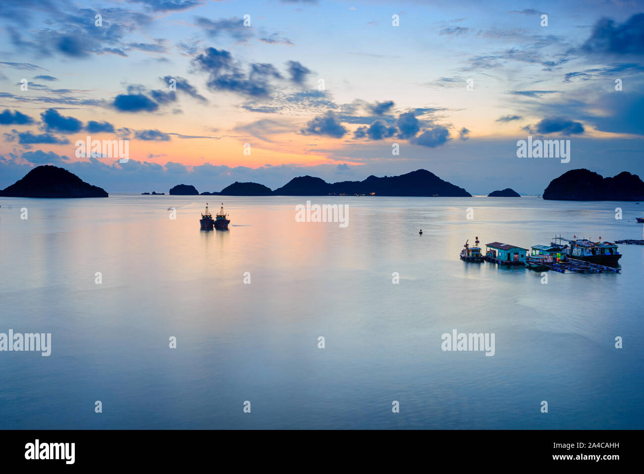Vietnam Cat Ba Bucht bei Sonnenuntergang mit schwebenden Fischerboote auf Meer, cloudscape tropische Wetter, bunte Himmel und Inseln am Horizont. Lange ex Stockfoto