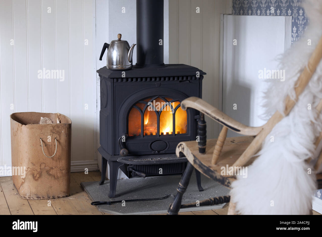 Skandinavischer Innenraum: Holzofen, Box von Brennholz und alten Schaukelstuhl in Wohnzimmer Ecke. Stockfoto