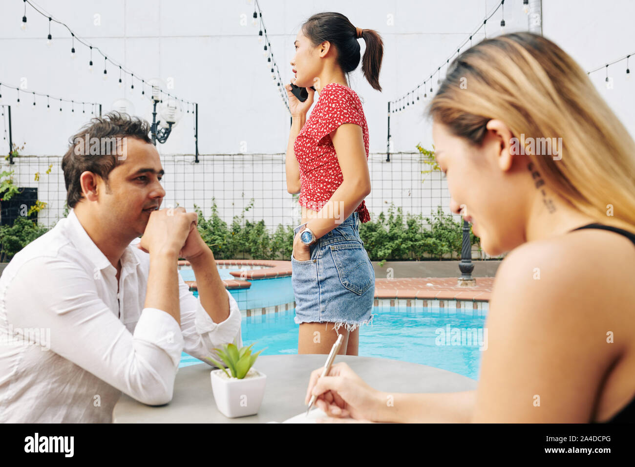 Digitale Nomaden Arbeiten durch den Pool: die Kolleginnen und Kollegen diskutieren, arbeiten und junge Frau ruft budinrdd Partner oder Kunde Stockfoto