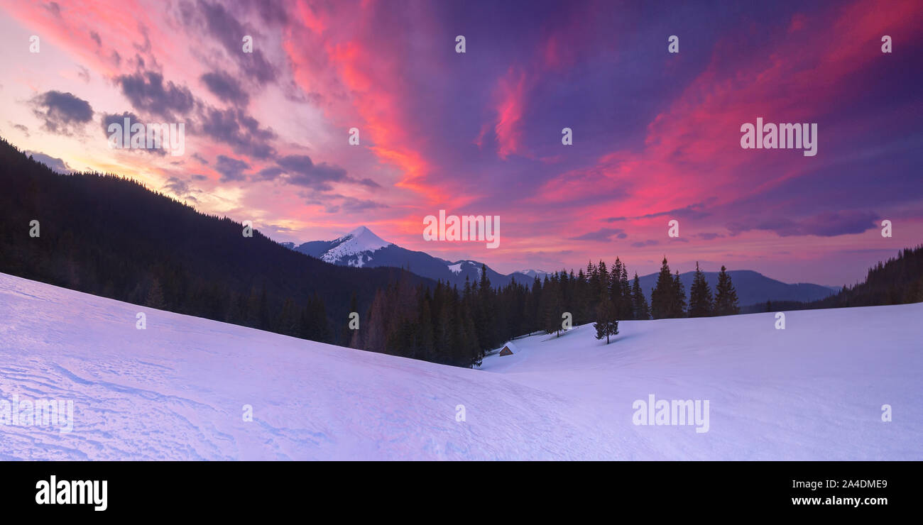 Traumhafte Winterlandschaft mit einem einsamen Haus in den Bergen. Sonnenuntergang mit schönen Wolken. Schneebedeckte Berggipfel Stockfoto