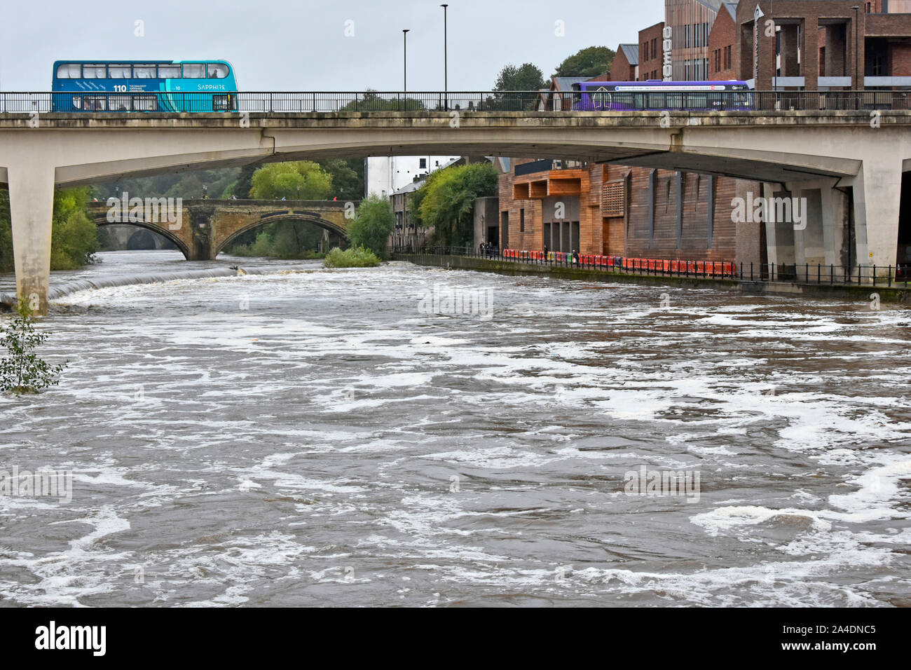 Konkrete Road Bridge & Busse Kreuzung oben turbulenten Fluss Wear nach heftigen Sommerregen historische arch Framwellgate Brücke jenseits Durham England Großbritannien Stockfoto