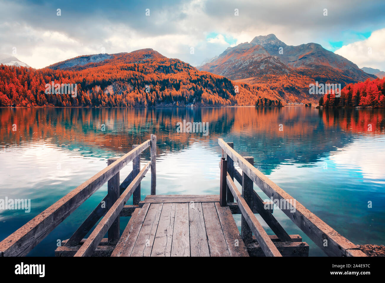 Hölzerne Seebrücke im Herbst den Silsersee (Silsersee) in den Schweizer Alpen. Snowy Mountains und Orangenbäumen im Hintergrund. Schweiz, Maloja Region Oberengadin. Landschaftsfotografie Stockfoto