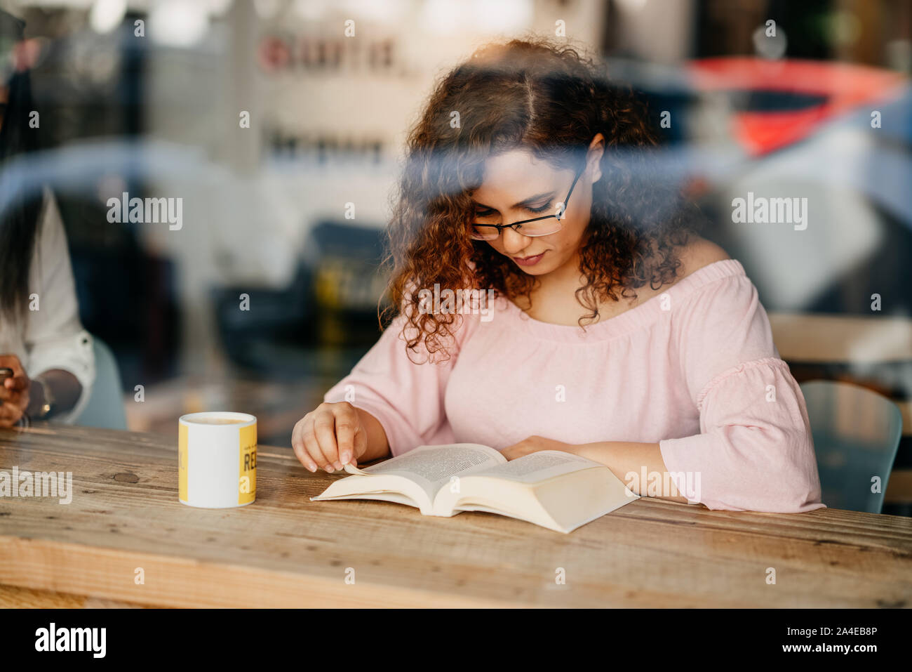 Junge Frau mit Brille Buch lesen im Cafe. Stockfoto