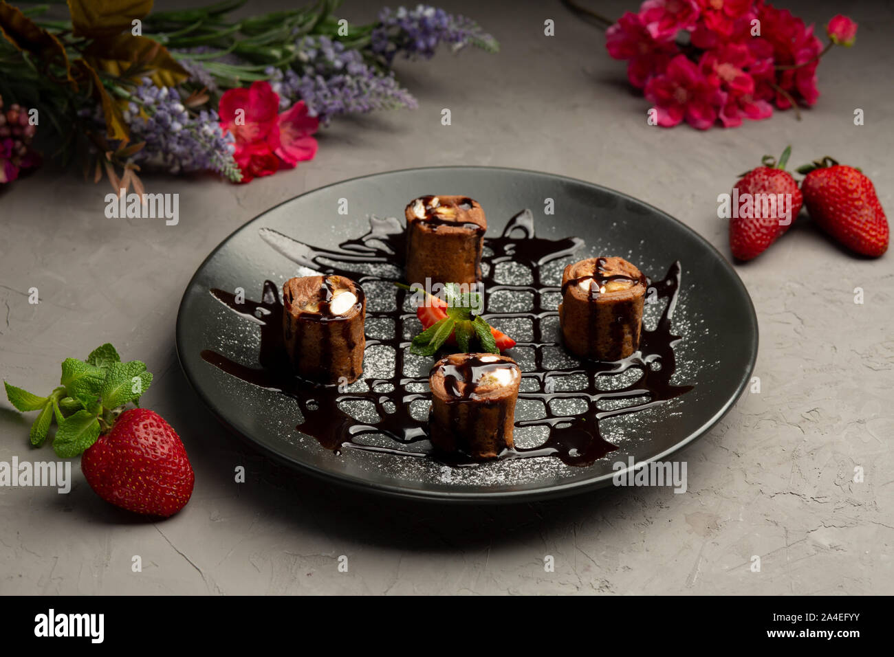 Süße roll-Schokolade Pfannkuchen, Erdbeeren, Banane, Orange, Butter Creme in einer schwarzen Platte auf grauem Hintergrund Stockfoto