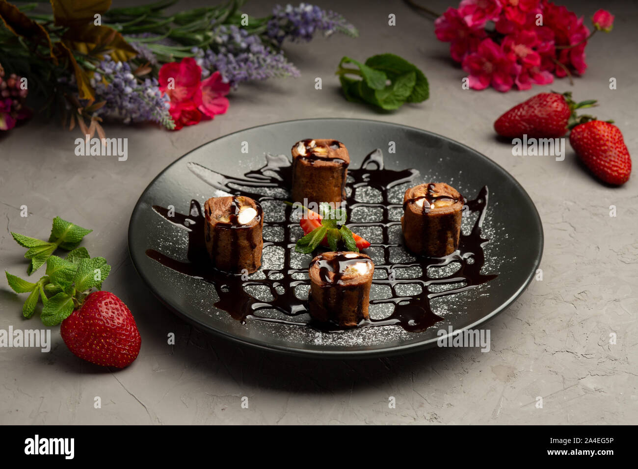 Süße roll-Schokolade Pfannkuchen, Erdbeeren, Banane, Orange, Butter Creme in einer schwarzen Platte auf grauem Hintergrund Stockfoto