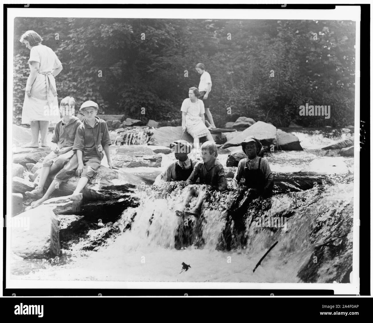 Drei Jungen im Creek sitzt, und drei Mädchen und zwei Jungen auf Felsen in Rock Creek, Washington, D.C. Stockfoto