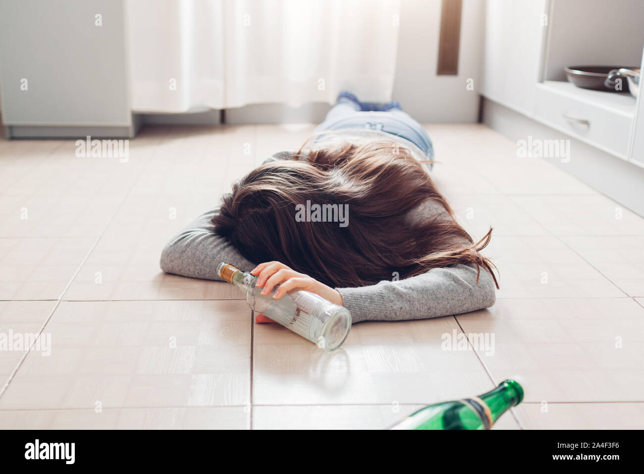 Weibliche Alkoholabhängigkeit. Junge Frau schlafen auf Küche Etage nach, die Flasche Stockfoto