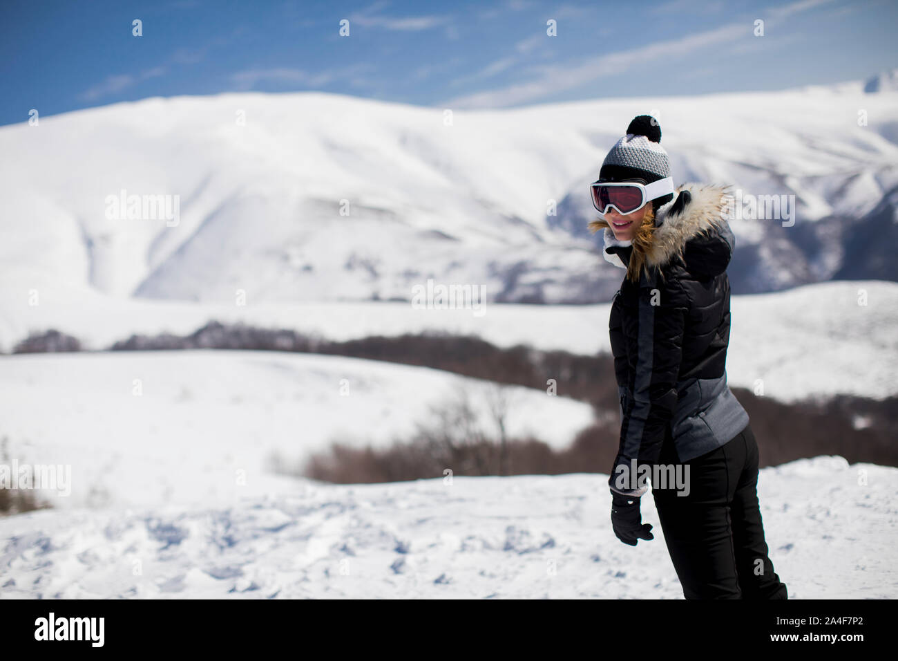 Junge Frau steht auf einem schneebedeckten Hang in Ihrer Ski Anzug in den Tag Stockfoto