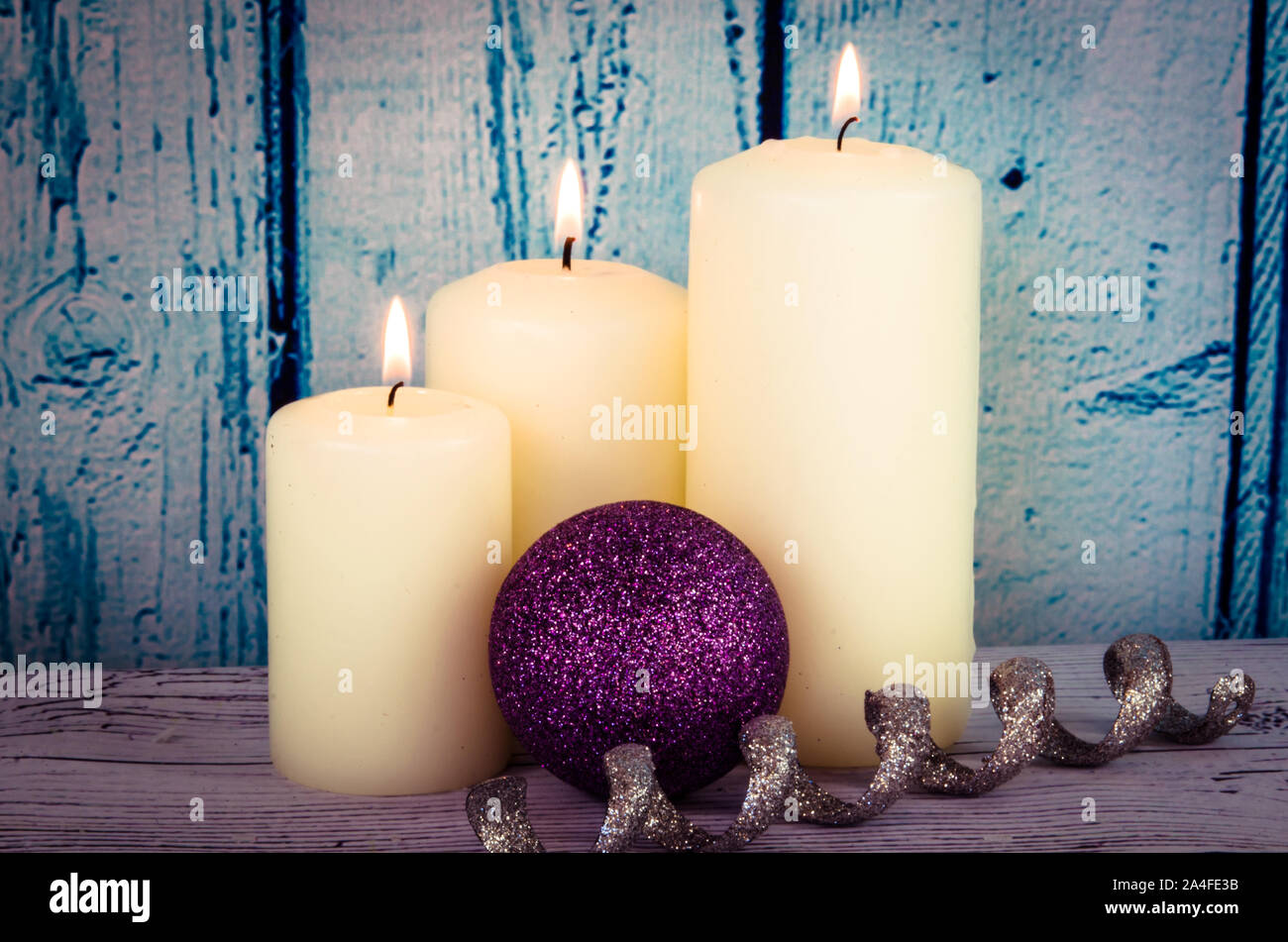 Brennende Kerzen weiß und lila Christbaumkugel Weihnachten Dekoration vor blauem Hintergrund Holz Stockfoto