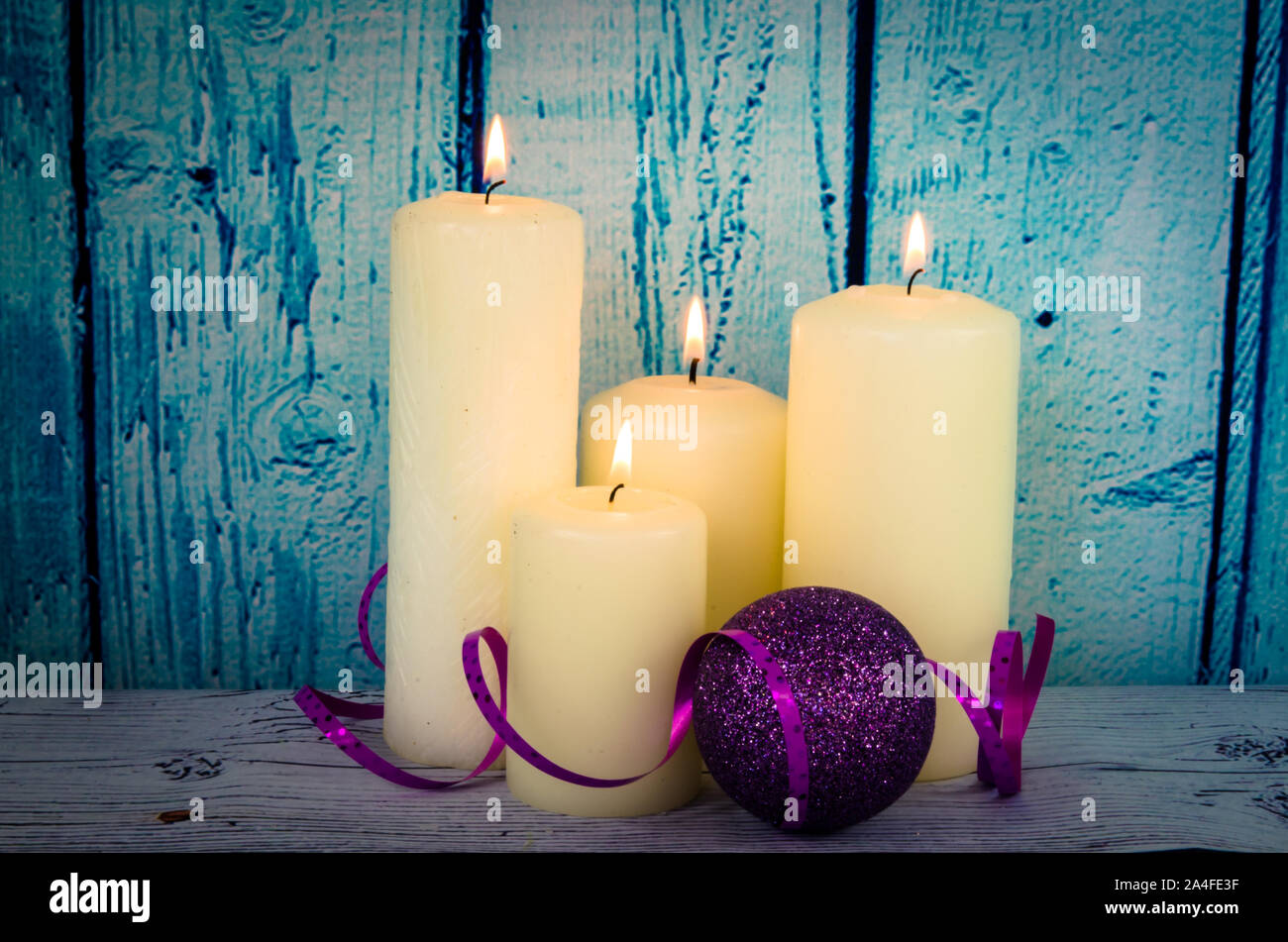 Brennende Kerzen weiß und lila Christbaumkugel Weihnachten Dekoration vor blauem Hintergrund Holz Stockfoto