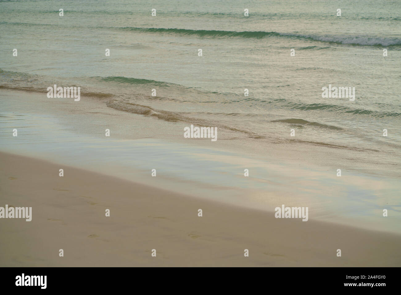 Sanfte Wellen am Strand am Morgen. Fading Fußspuren im Sand in warmen Pastellfarben. Atmosphärische Konzept Hintergrund für Reise und Tourismus. Stockfoto