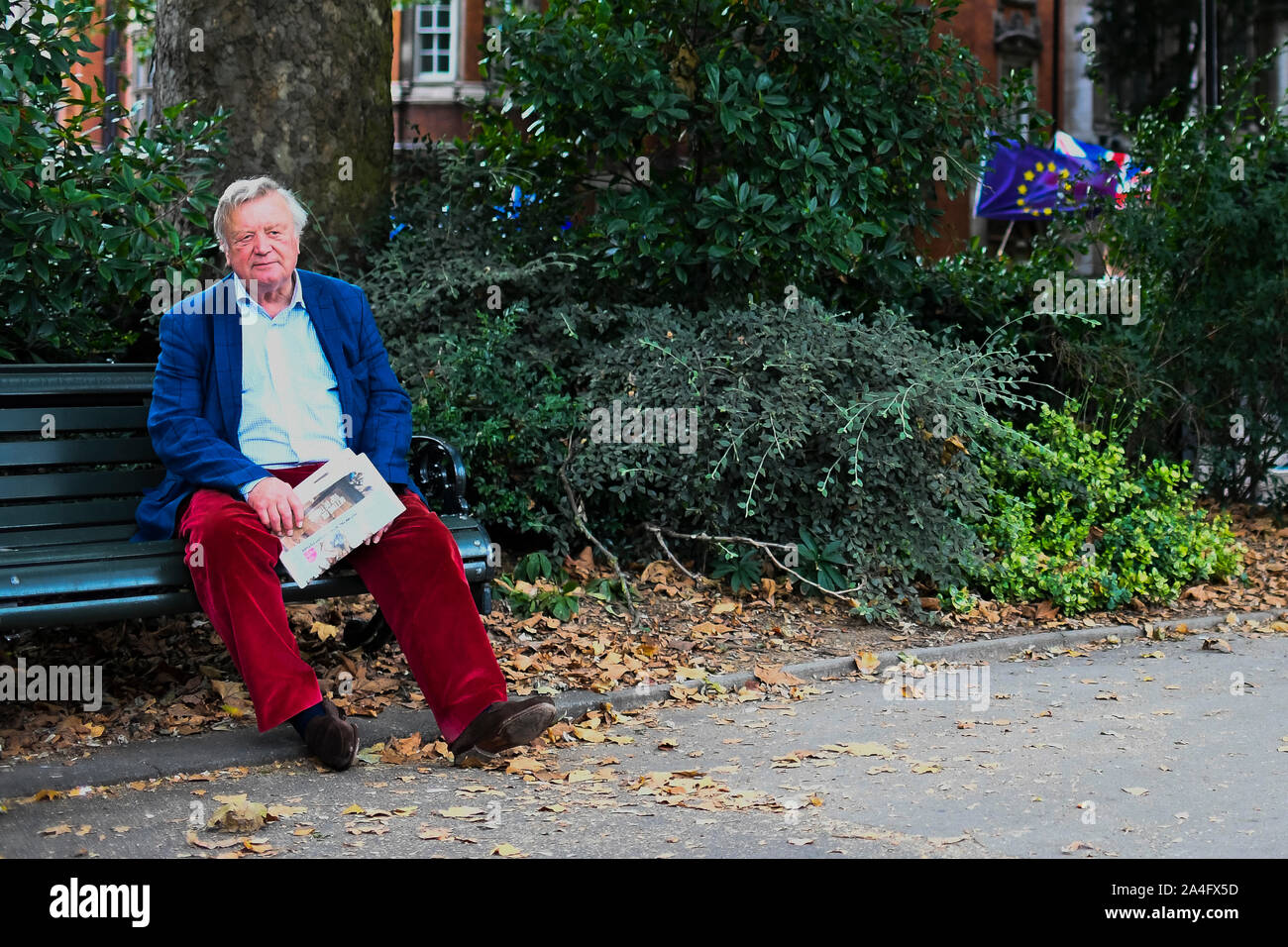 London, Großbritannien. Politiker Ken Clarke sitzt auf einer Bank in Victoria Tower Gardens mit europäischen Flaggen im Hintergrund. Stockfoto