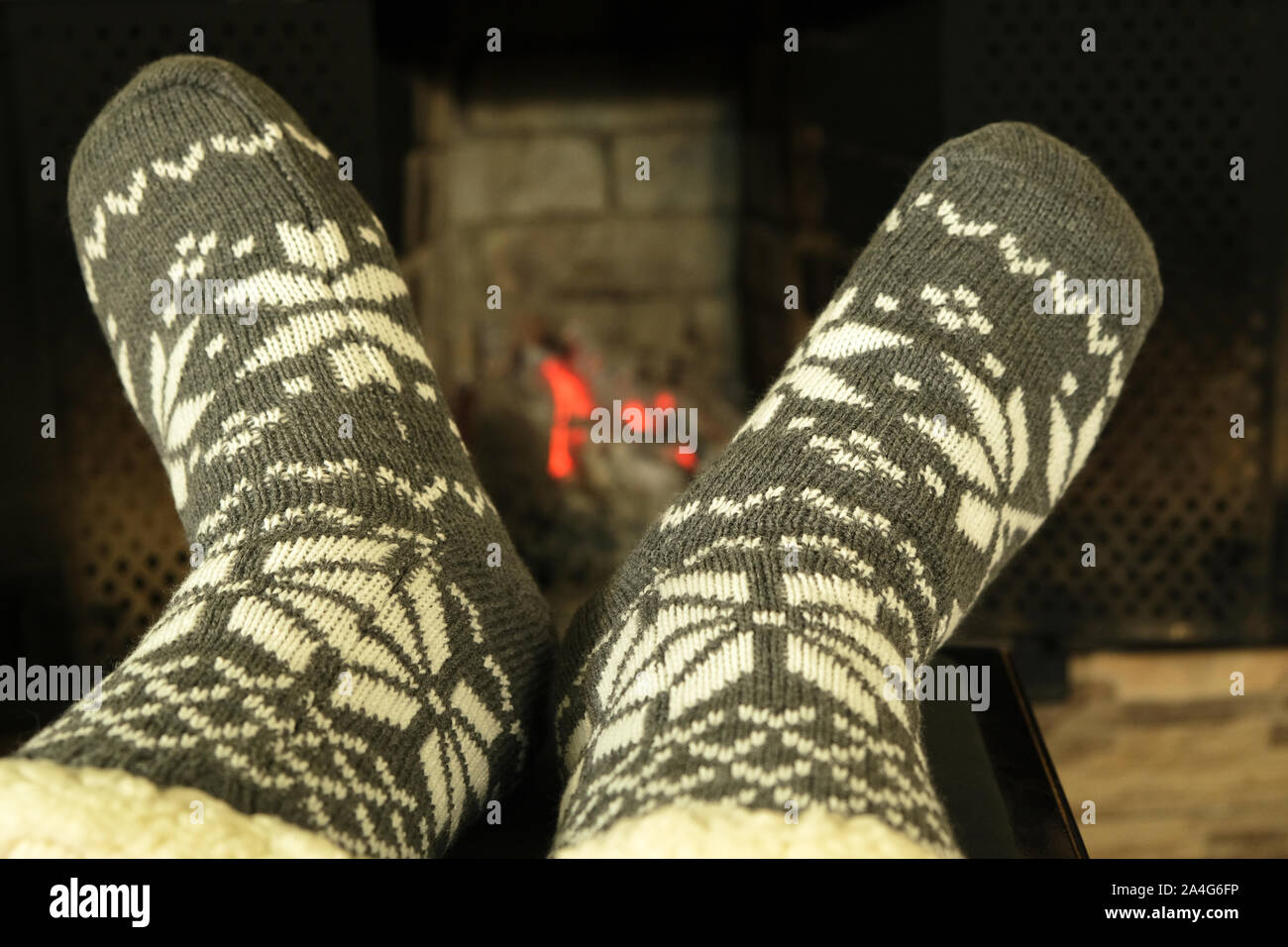 Füße im kammgarn winter Socken mit weißer Ornament am Kamin im Winter abends, Konzept der entspannenden gemütlichen Neues Jahr Nacht und Weihnachten im Hause Stockfoto