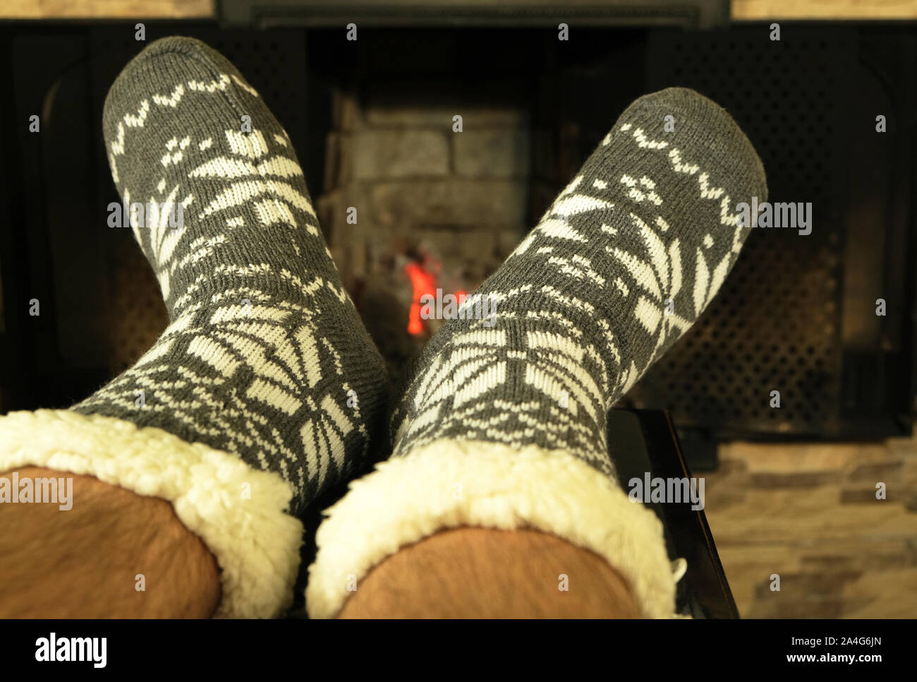 Männliche haarige Füße in Wolldecken warme Socken mit weißer Ornament in der Nähe der Kamin im Winter abends, das Konzept einer entspannenden gemütlichen Weihnachten Nacht zu Hause Stockfoto